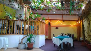 A restaurant with a wooden railing, tables with white tablecloths, and potted plants.