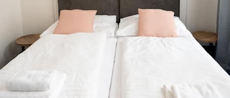 Una cama doble con ropa de cama blanca y almohadas color melocotón, dos mesitas de noche y un cabecero gris.