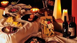 A table set with food and wine, candles, and a city view at night. - Su Lithu (Bitti)
