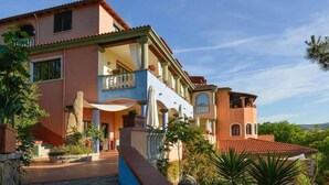 A multi-story house with a balcony, a stone wall, and a red-tiled roof. - Su Lithu (Bitti)