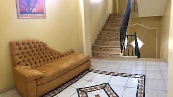 Una sala de estar con un sofá marrón, un tapete estampado y una escalera con barandilla.