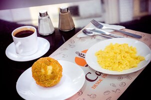 Un desayuno con huevos revueltos, un croissant y una taza de café sobre una mesa, con servilleta y cubiertos.
