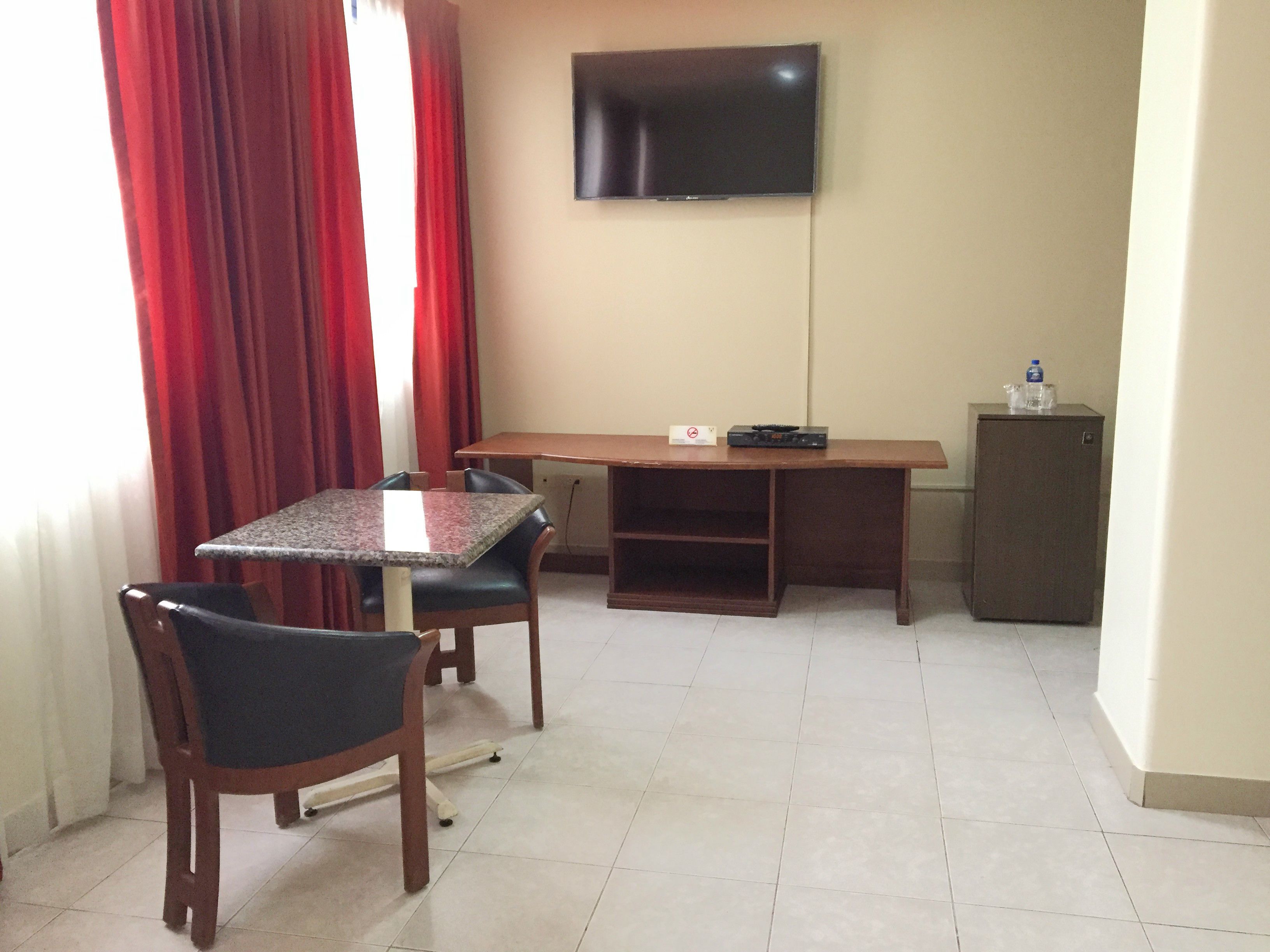 Una habitación con una mesa de comedor, dos sillas, un televisor montado en la pared y un refrigerador pequeño.