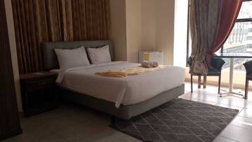 A hotel room with a bed, a nightstand, a window with curtains, and a view of the city.