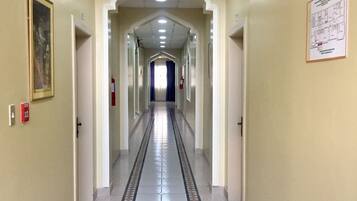 A long, narrow hotel corridor with a tiled floor, a fire extinguisher, and a 'SALIDA' sign on the wall.
