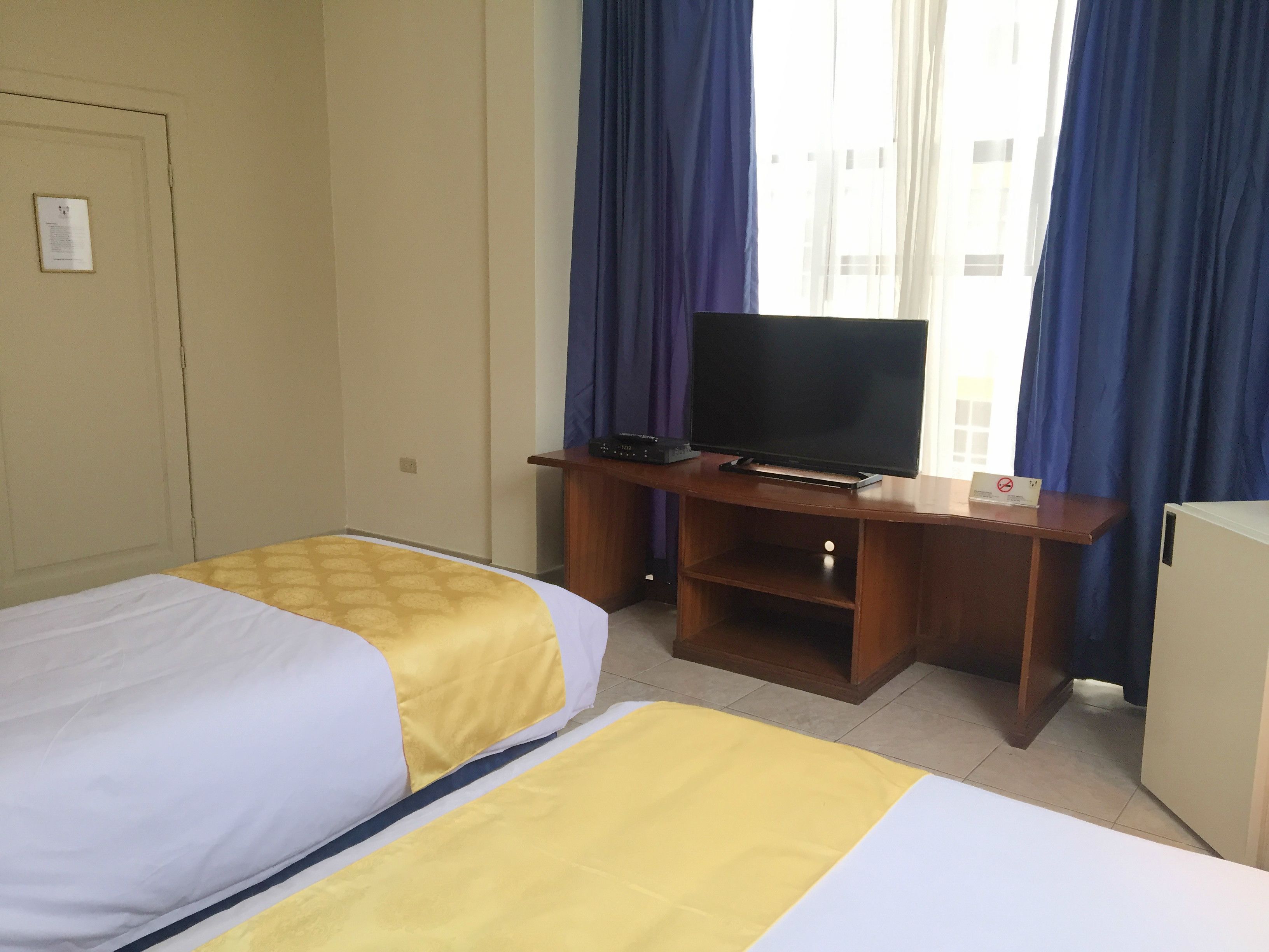 Hotellihuone, jossa on kaksi sänkyä, televisio puutelineessä ja pieni jääkaappi.
