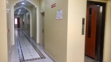 Un pasillo de hotel con suelo de baldosas, un detector de incendios y un ascensor.