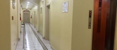 A long, narrow hallway with a tiled floor, a fire extinguisher, and a sign indicating the exit direction.