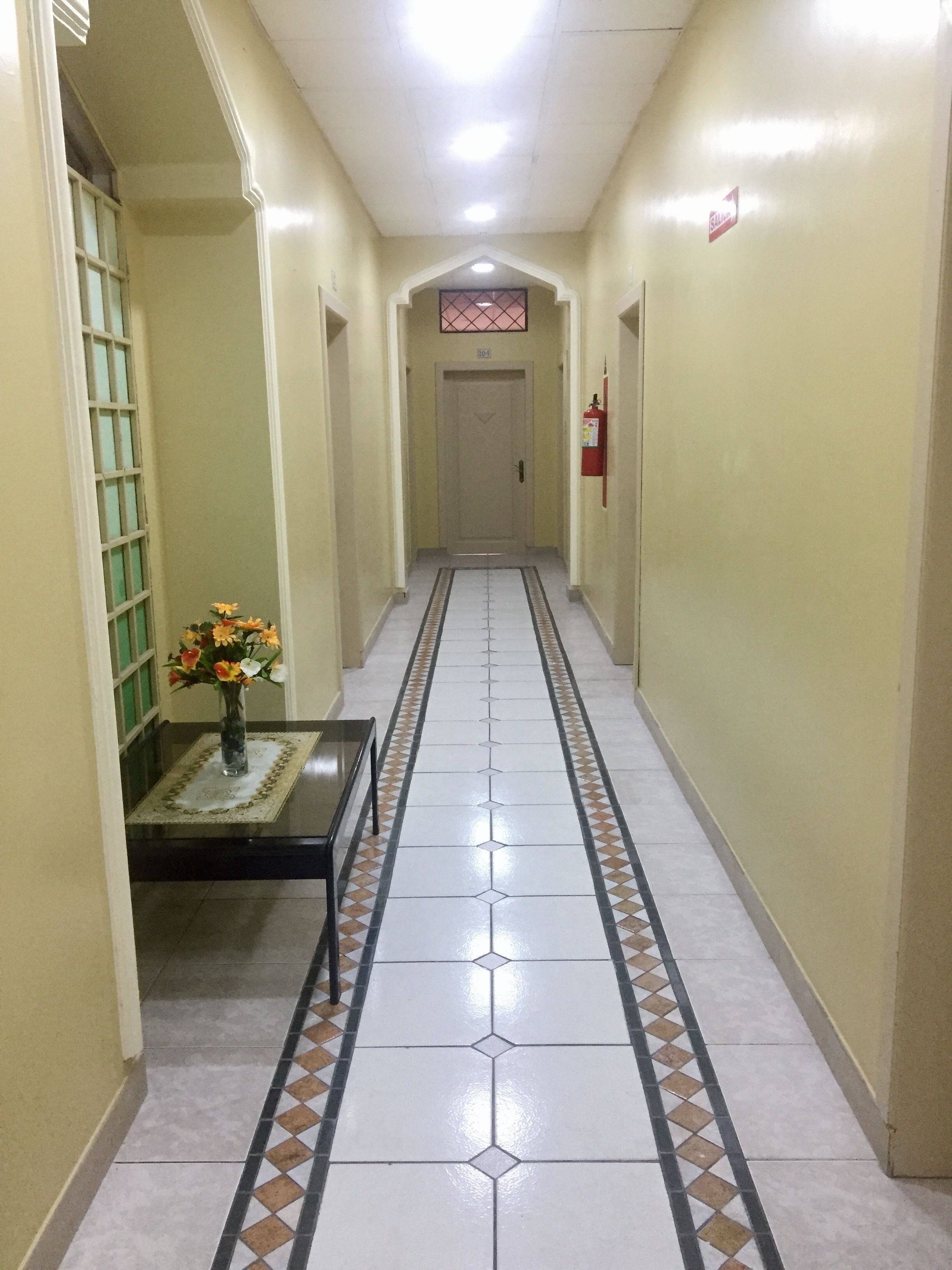 A hallway with a tiled floor, a fire extinguisher, and a door at the end.