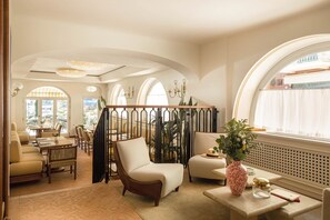 Ein geräumiger Lounge-Bereich mit bequemen Sitzmöglichkeiten, einer dekorativen Vase und Blick durch große Bogenfenster.