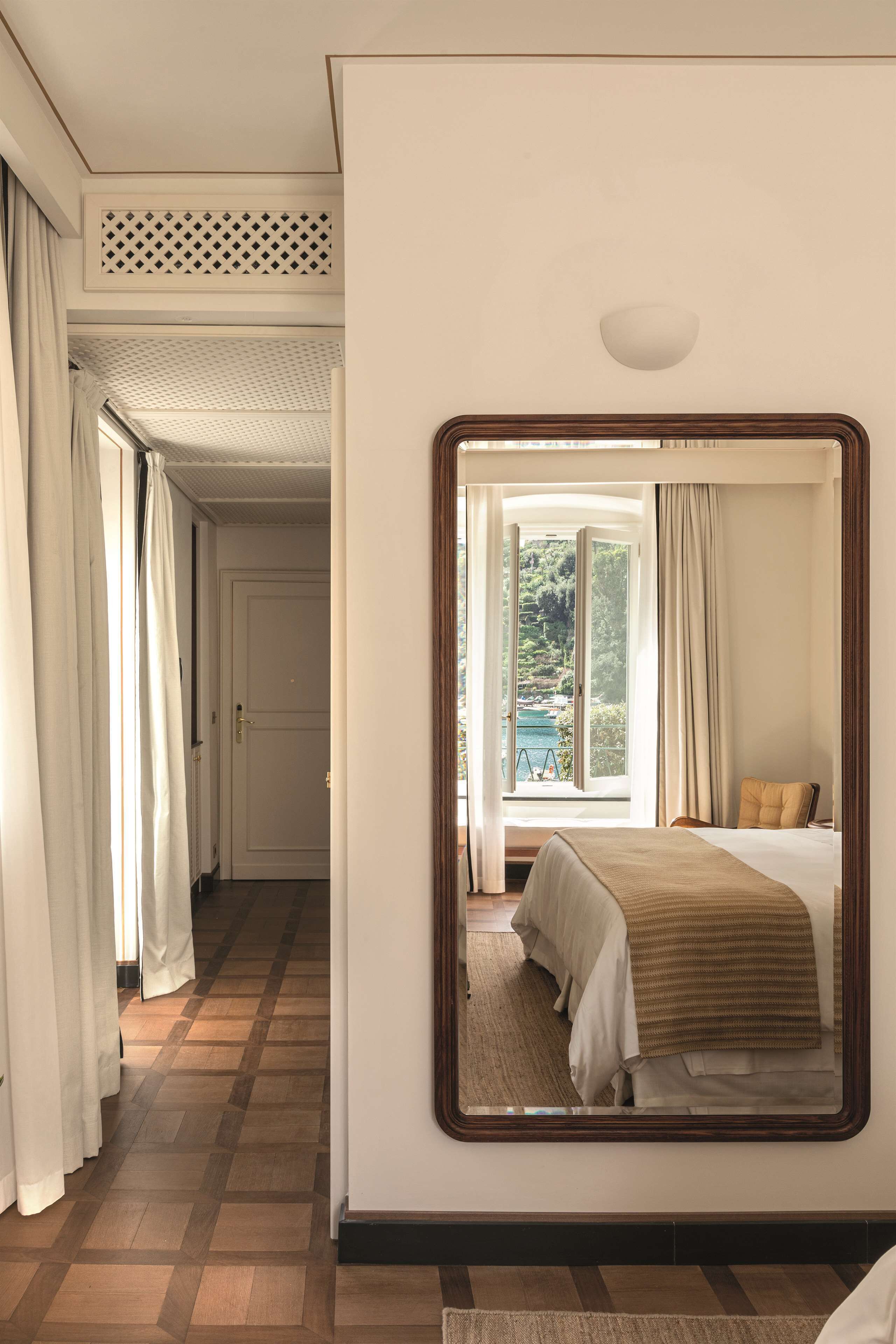 Habitación de hotel con un espejo grande, una cama, una ventana con vista a zonas verdes y piso de madera.