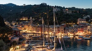 Un pueblo costero con un puerto deportivo lleno de veleros e yates, rodeado de edificios coloridos y una colina al fondo.