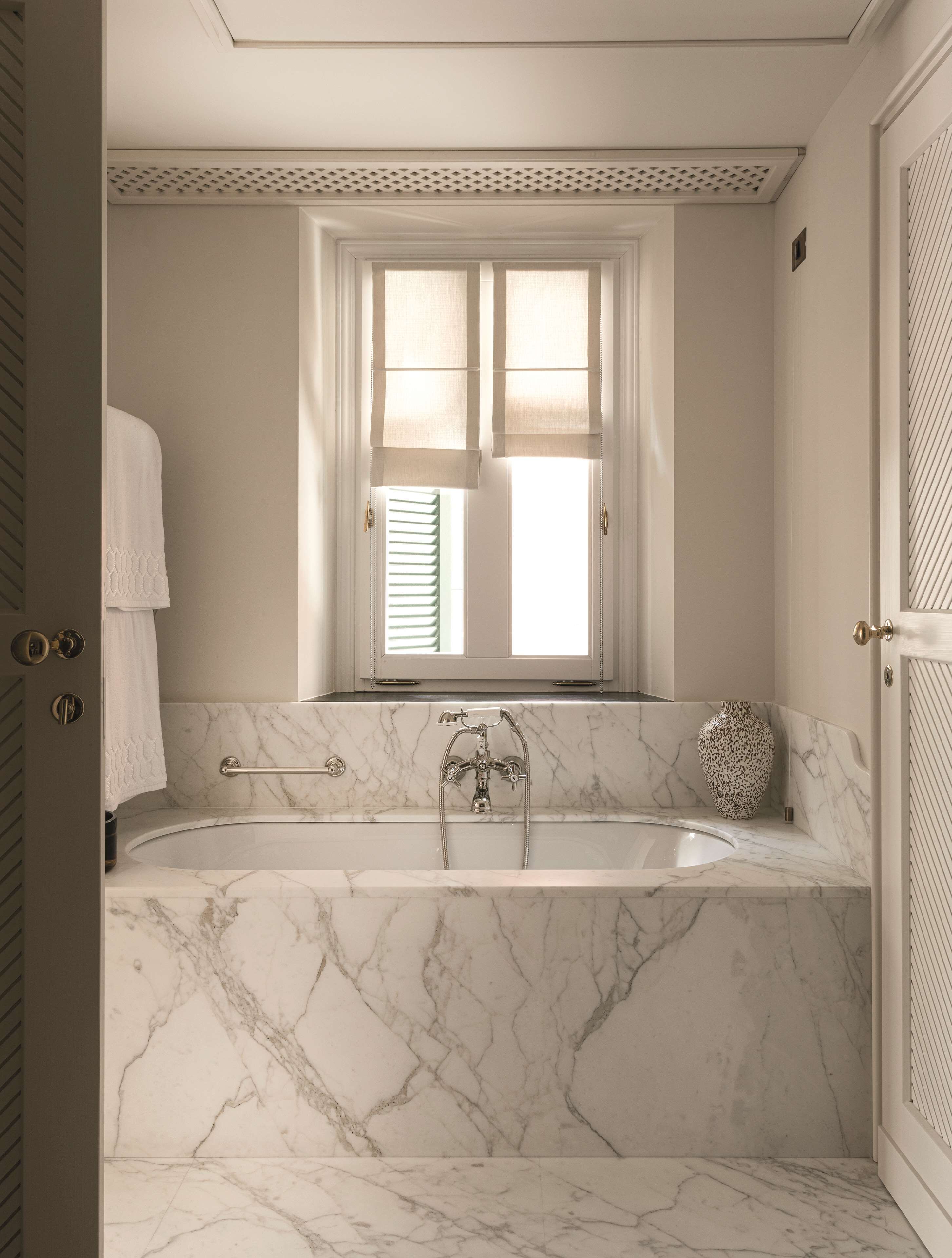 A bathroom with a marble bathtub, a window with blinds, and a towel rack.