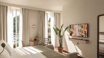 Una camera d'albergo con un letto, una sedia, un tavolino, una pianta in vaso, una televisione e un balcone con vista.