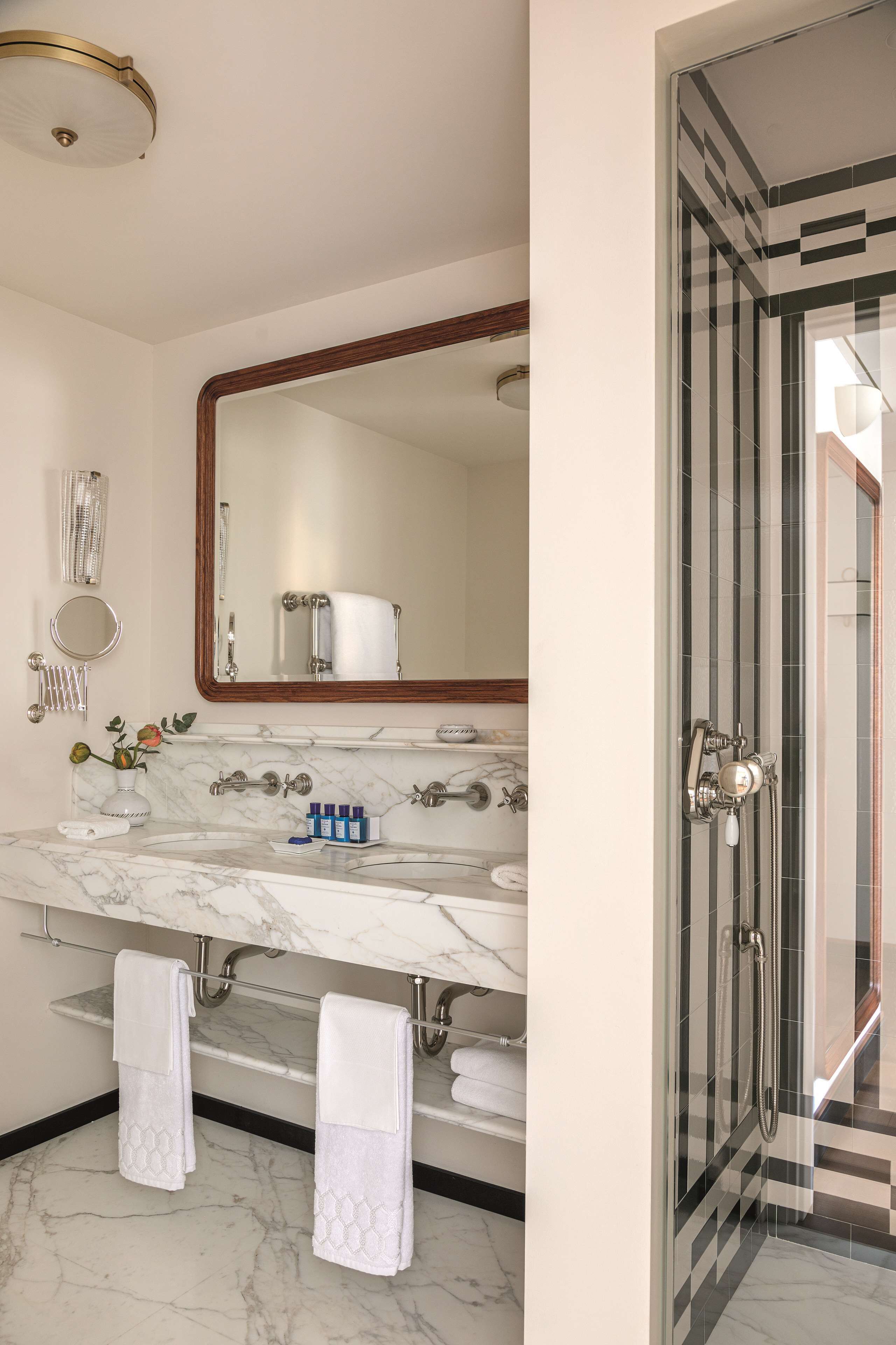 A bathroom with a marble sink, a large mirror, a shower with a glass door, and towels hanging on a rack.