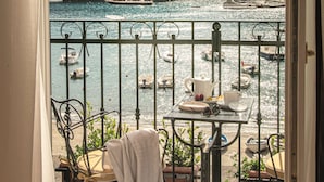 Un balcón con vista al puerto, una mesa con una tetera y una silla con una manta.