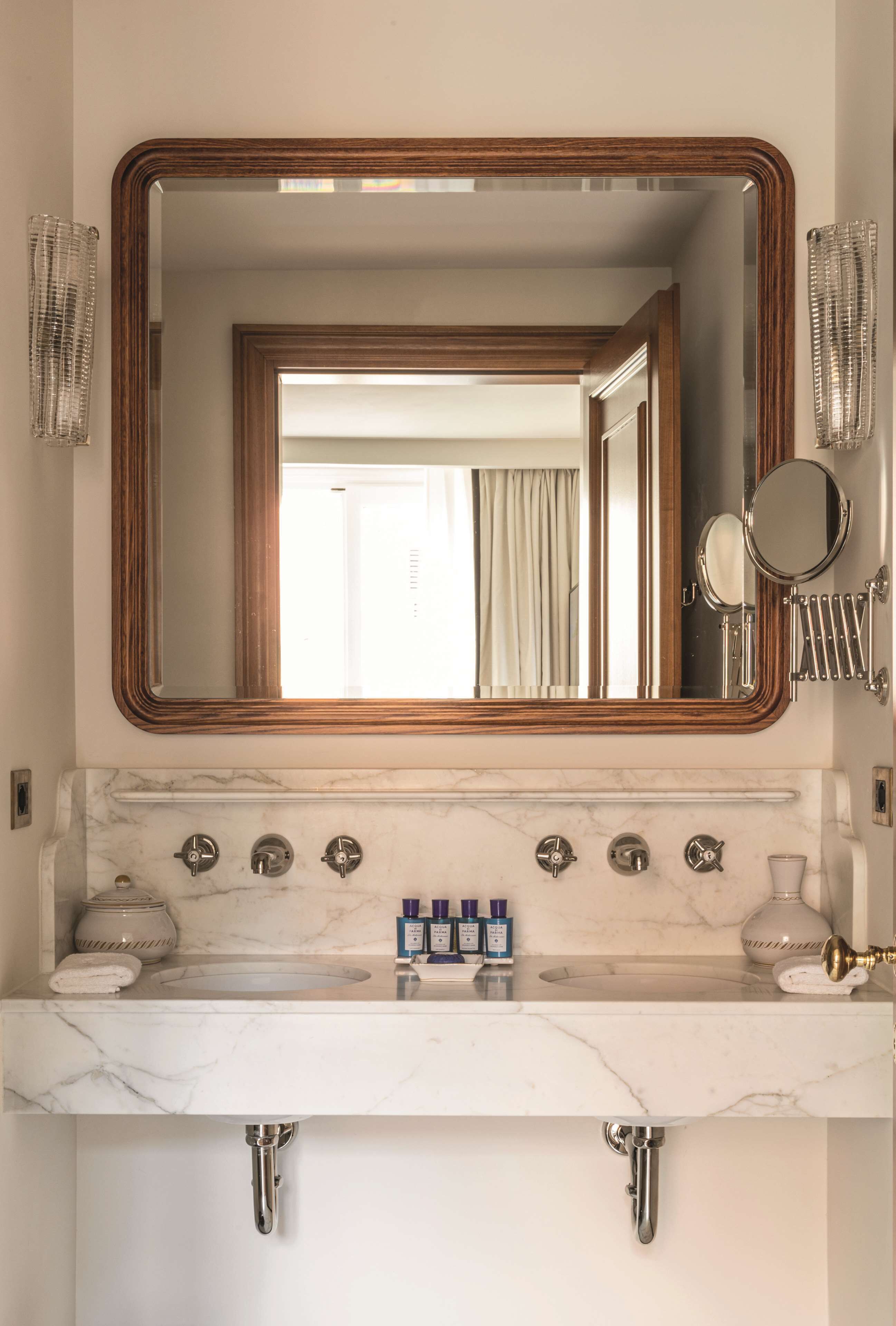 Un bagno con lavabo in marmo, diversi rubinetti, uno specchio grande e un portascopevoli.
