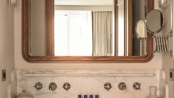 Un bagno con lavabo in marmo, diversi rubinetti, uno specchio grande e un portascopevoli.