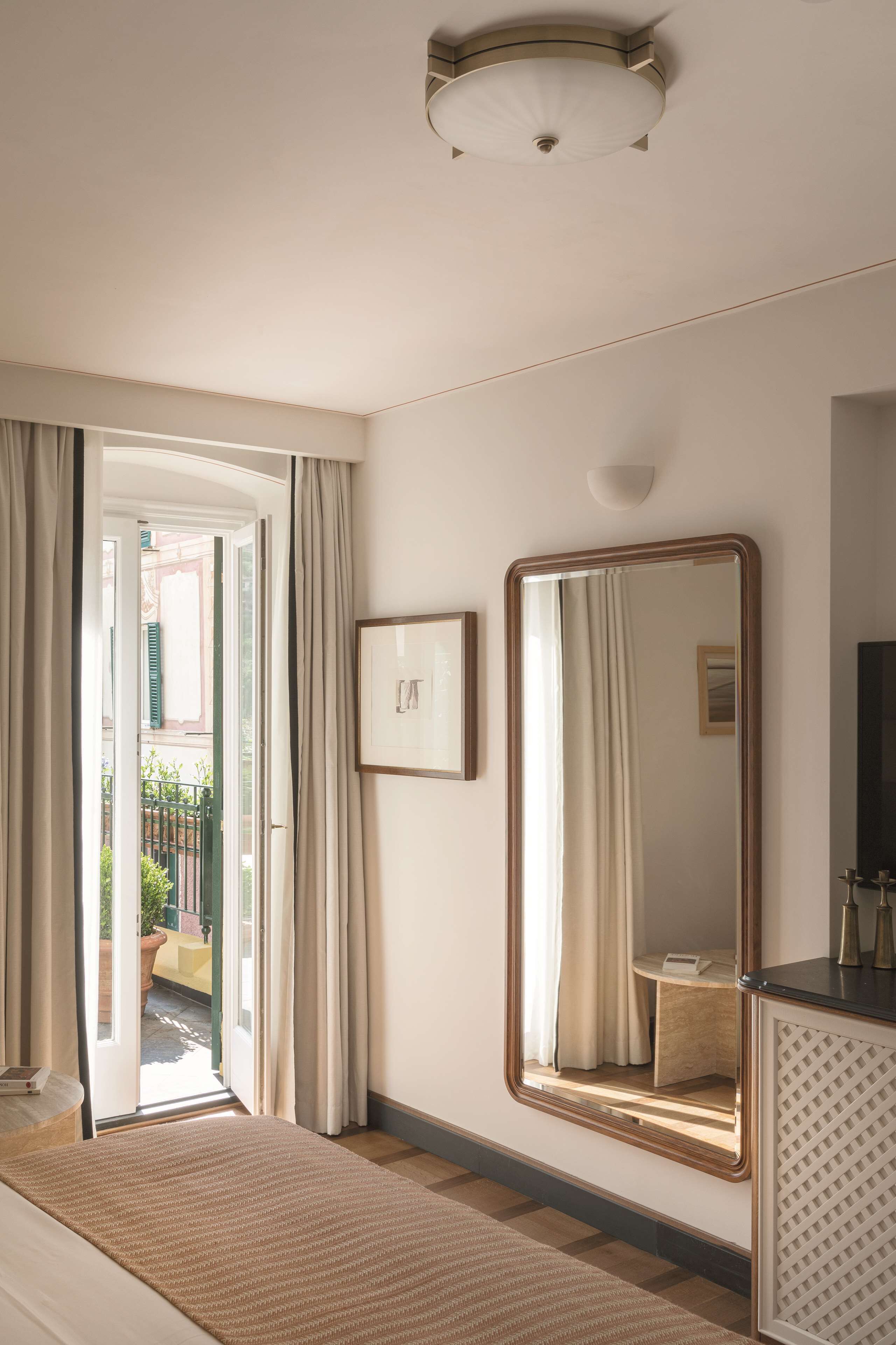 Une chambre d’hôtel avec un lit, un grand miroir, un tableau encadré et une vue sur l’extérieur par une porte ouverte.