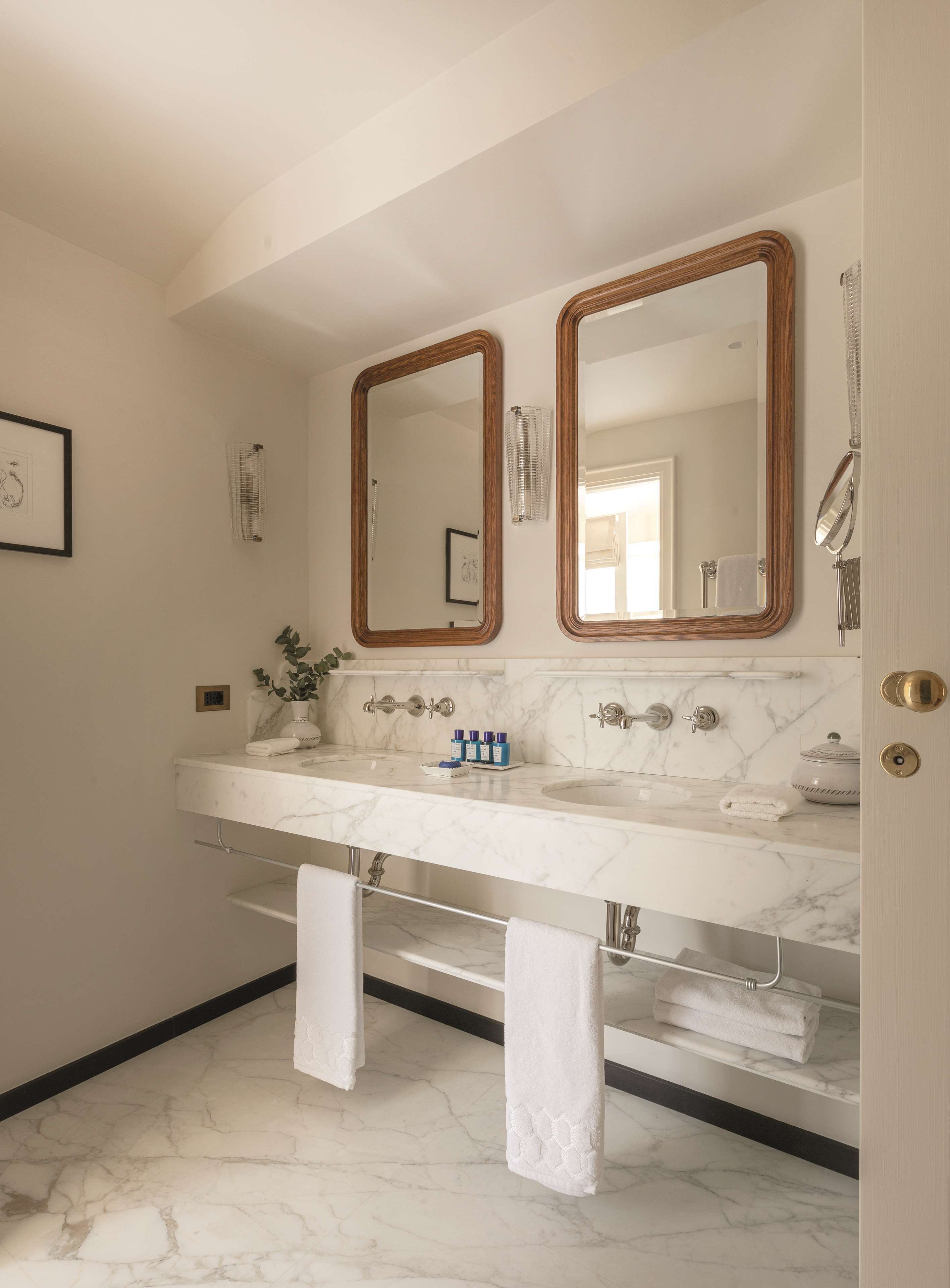 A bathroom with a marble countertop, two mirrors, a towel rack, and a door with a brass handle.