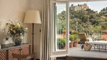 Ein Zimmer mit Esstisch, Stühlen, einer Vase mit Blumen, einer Lampe und Blick auf einen Balkon mit Gartenmöbeln sowie eine Burg im Hintergrund.