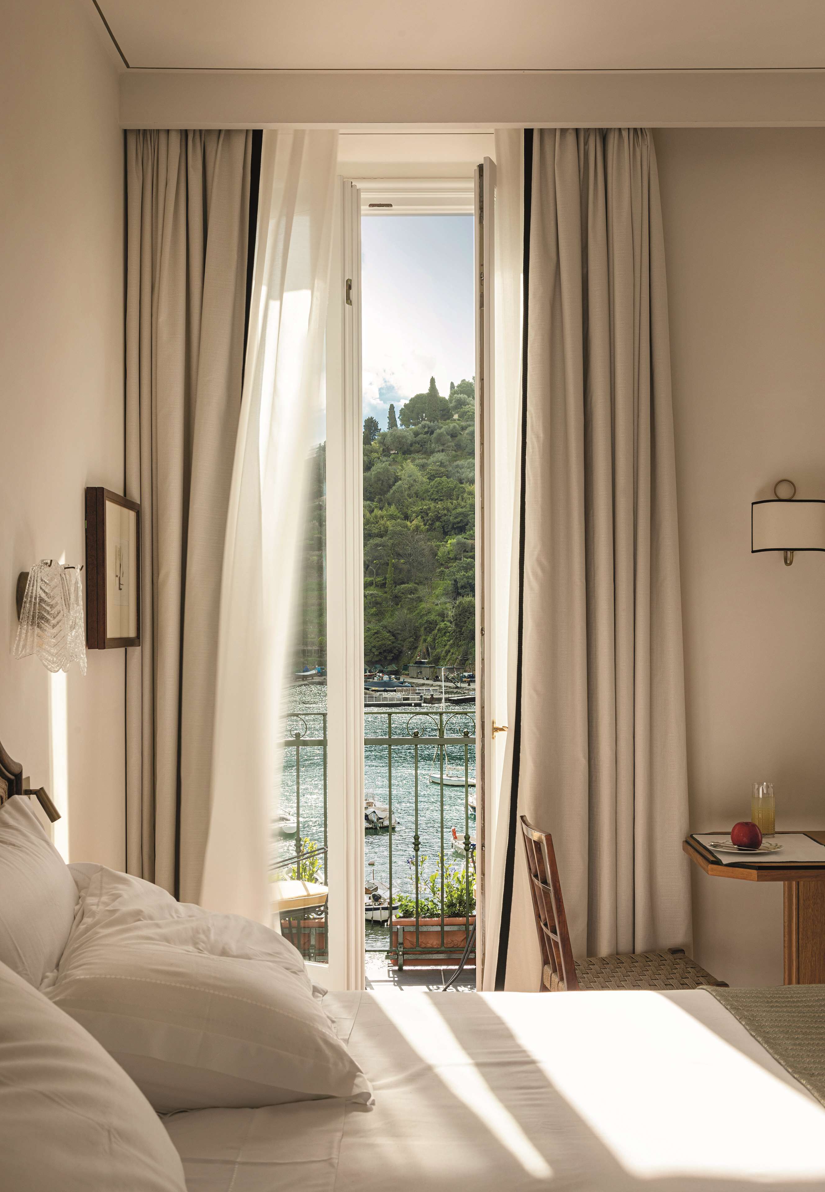 Une chambre d’hôtel avec un lit, une petite table sur laquelle se trouve un objet rouge, une chaise et une vue sur une étendue d’eau et de la verdure.