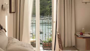 Une chambre d’hôtel avec un lit, une petite table sur laquelle se trouve un objet rouge, une chaise et une vue sur une étendue d’eau et de la verdure.