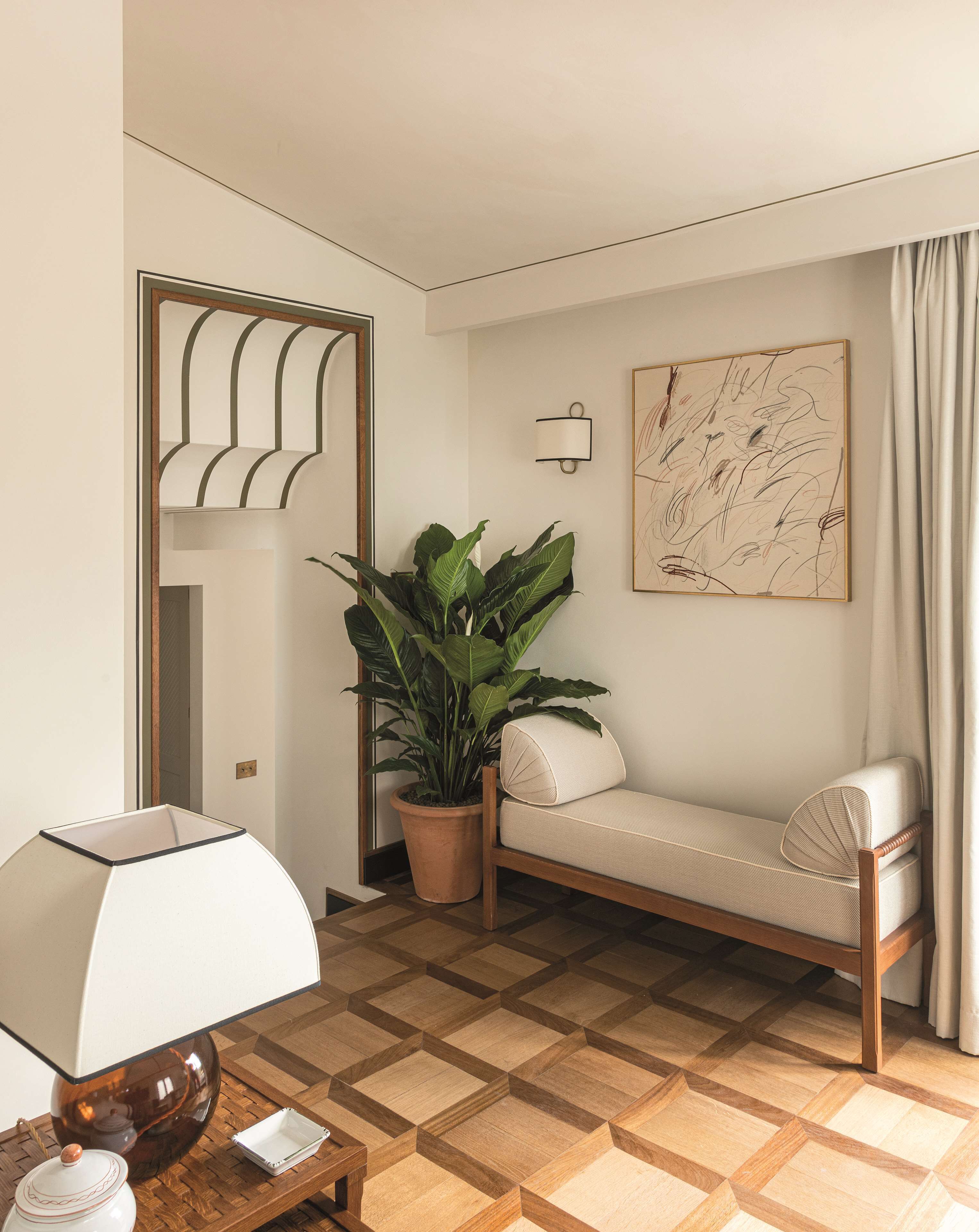 Quarto com sofá, planta em vaso, luminária, luz embutida na parede e piso com padrão geométrico.