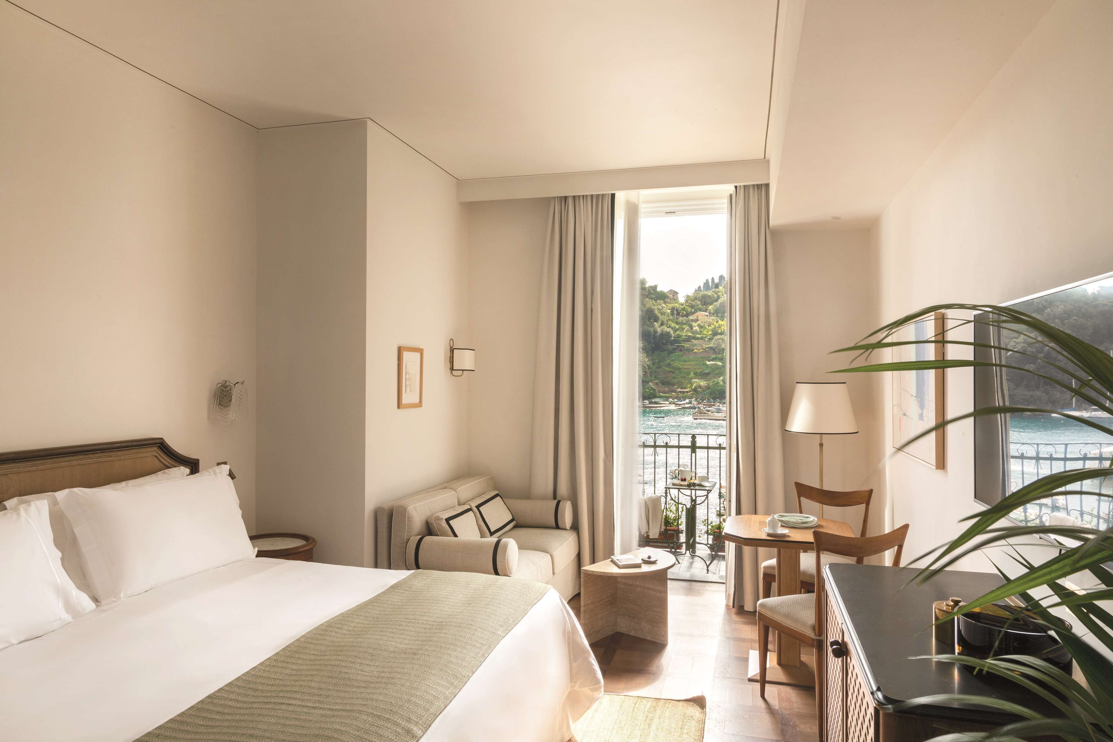 A hotel room with a bed, a sofa, a small table, a chair, and a view of the sea.