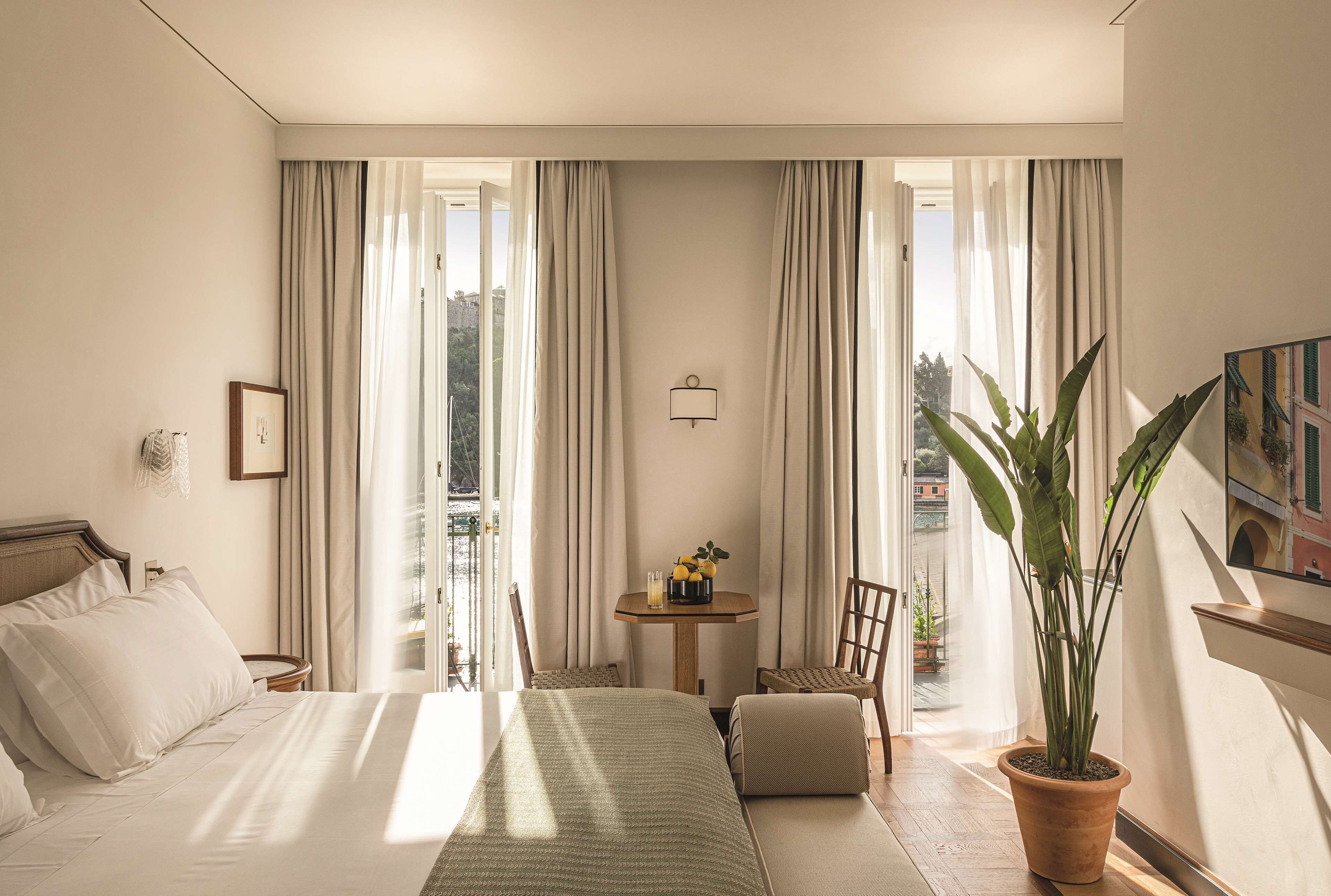Ein Hotelzimmer mit einem Bett, einem kleinen Tisch mit einer Vase, einem Sessel und einer Topfpflanze.