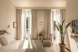 A hotel room with a bed, a small table with a vase, a chair, and a potted plant.