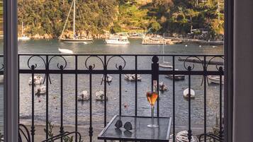 Un balcone con tavolo e sedie affacciato su uno specchio d'acqua, con barche e un castello su una collina.