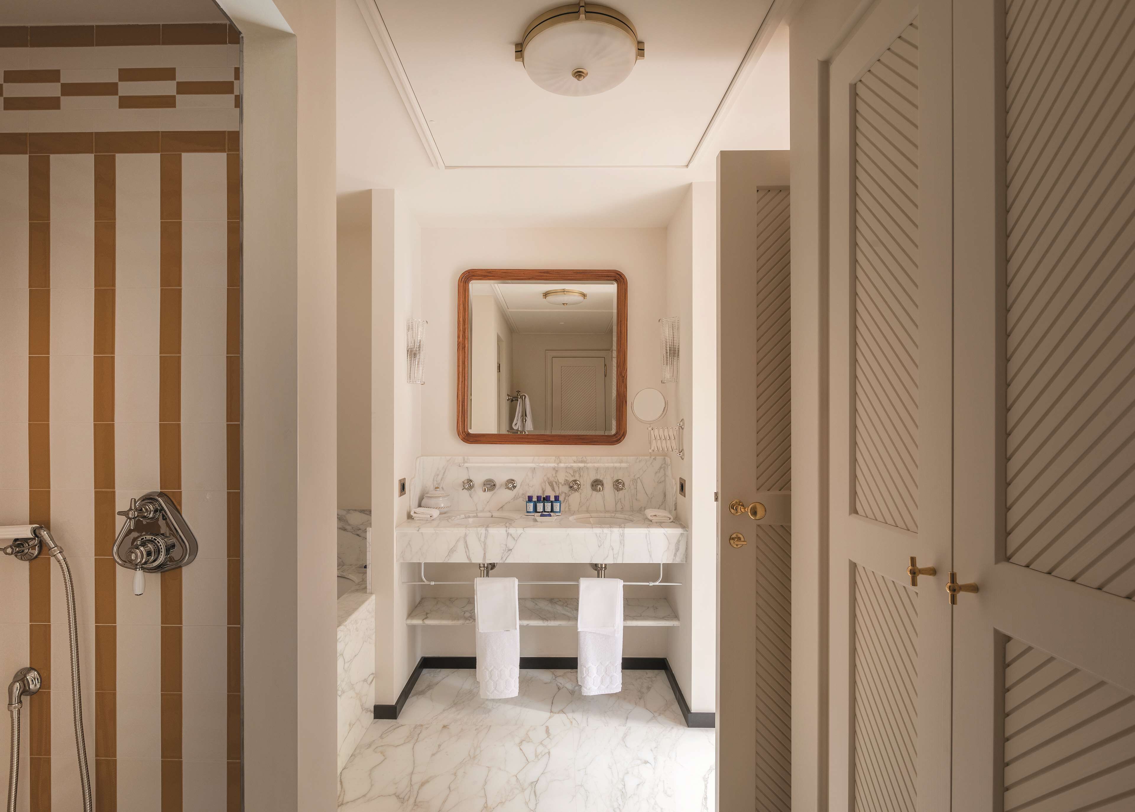 A bathroom with a marble sink, a large mirror, and a shower with a striped tile design.