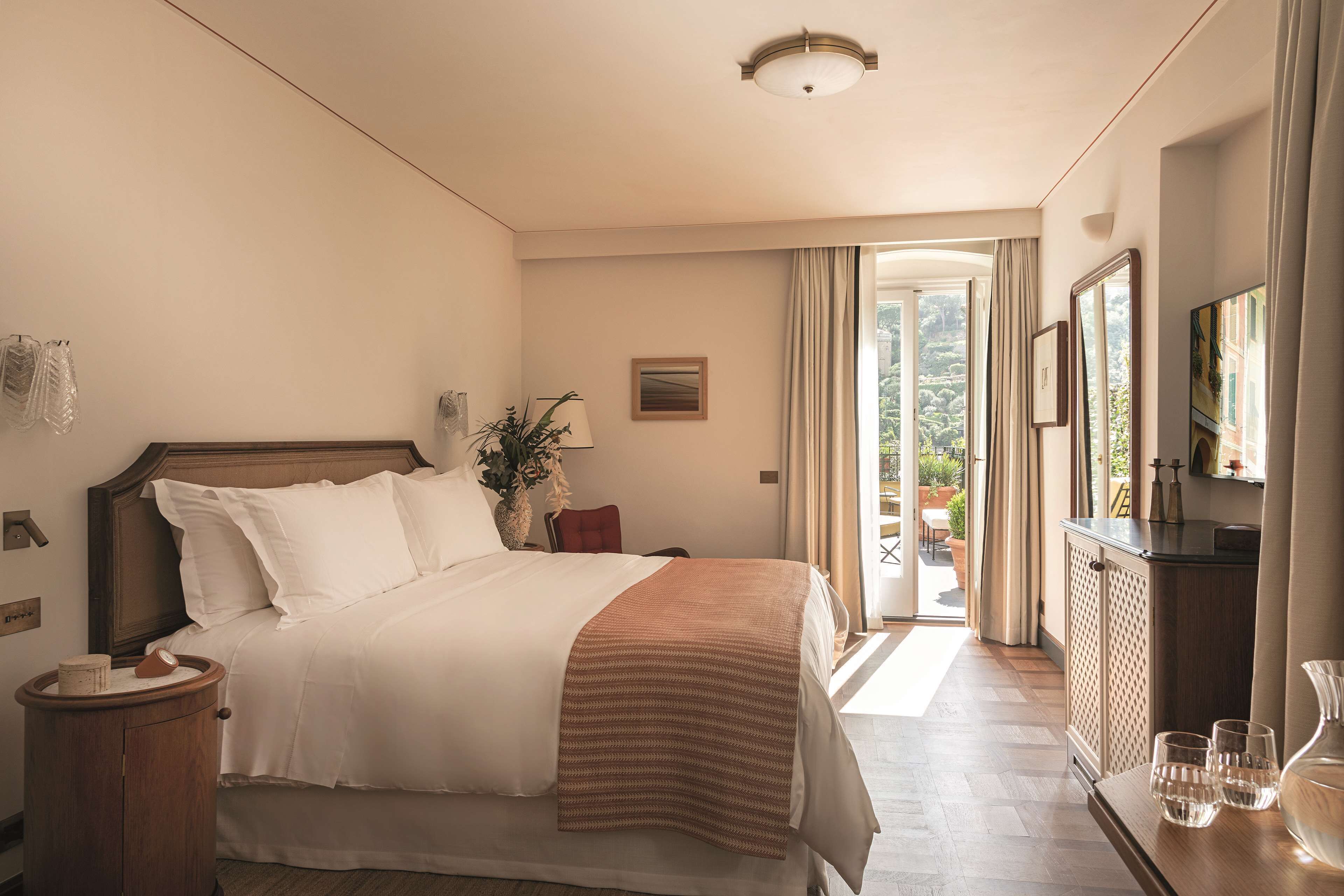 A hotel room with a large bed, a bedside table, a dresser, and a view of the outdoors.