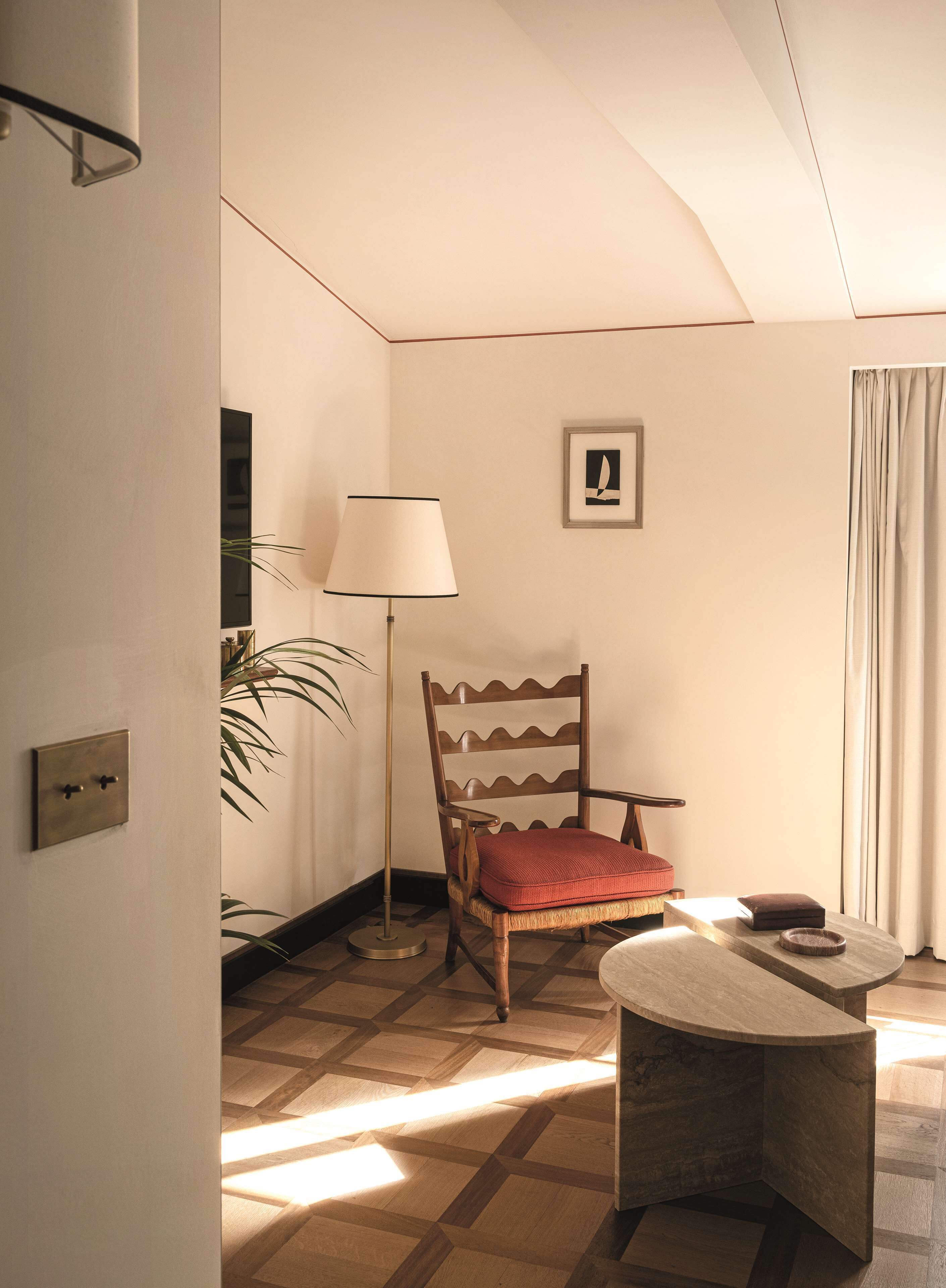 Una habitación con una silla de madera, una mesa, una lámpara y un cuadro en la pared.