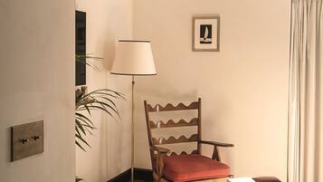 Una habitación con una silla de madera, una mesa, una lámpara y un cuadro en la pared.