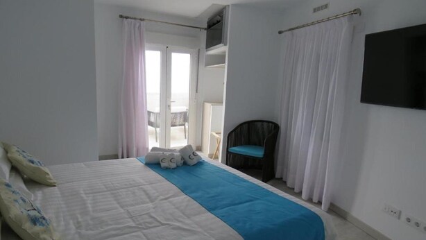 Un dormitorio con cama, una silla, un televisor y una puerta que da a un balcón.