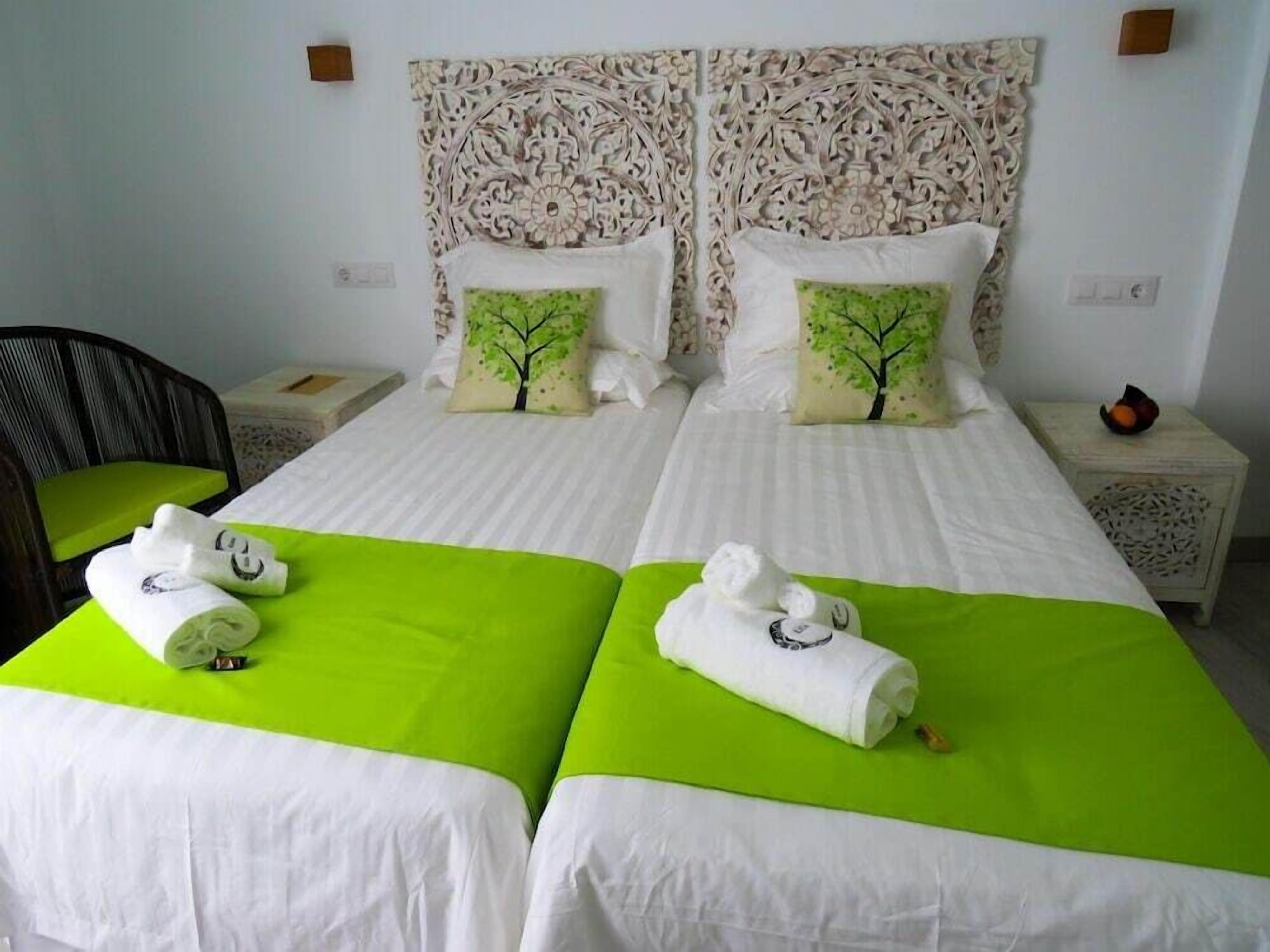 A hotel room with two single beds, each with a green bedspread and white linens, and matching decorative pillows.