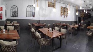 Un interior de restaurante con mesas y sillas de madera, arte decorativo en las paredes y lámparas colgantes.