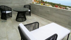 Una terraza con una mesa redonda y dos sillas, un sofá, y vistas a un pueblo en la ladera.