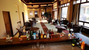 A bar area with a variety of liquor bottles and glasses, wicker furniture, and large windows allowing natural light.