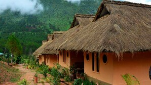 A row of thatched-roof houses with a garden pathway leading to them, set against a mountainous backdrop.