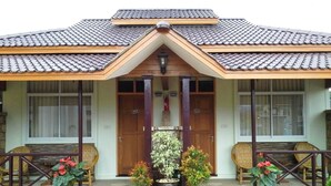 Une maison traditionnelle avec un toit en tuiles, une entrée centrale dotée d’une porte en bois et des plantes en pot devant la façade.