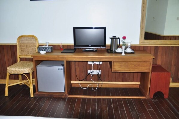 A wooden desk with a television, a small refrigerator, and a coffee maker.