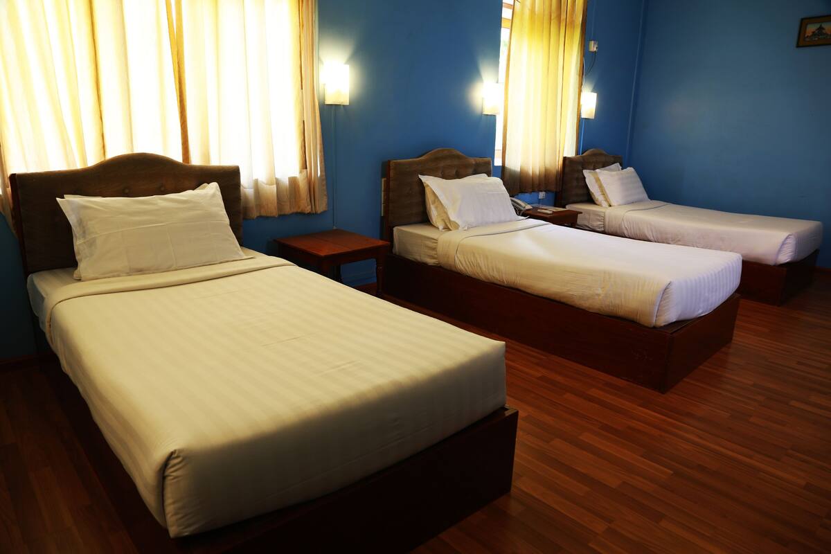 Ein Hotelzimmer mit zwei Einzelbetten, Holzboden und Vorhängen an den Fenstern.