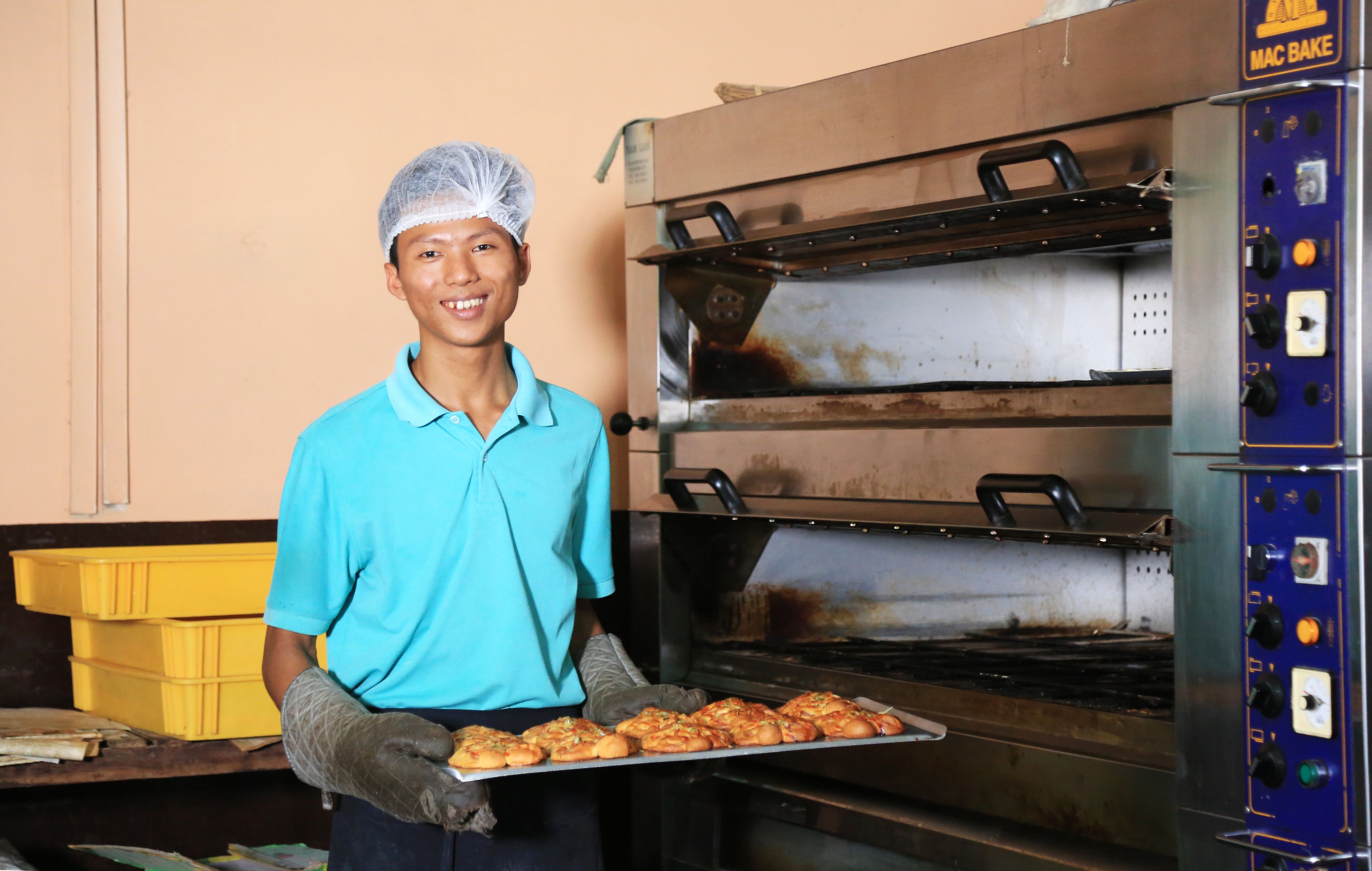 A person holding a tray of baked goods in front of a commercial oven.