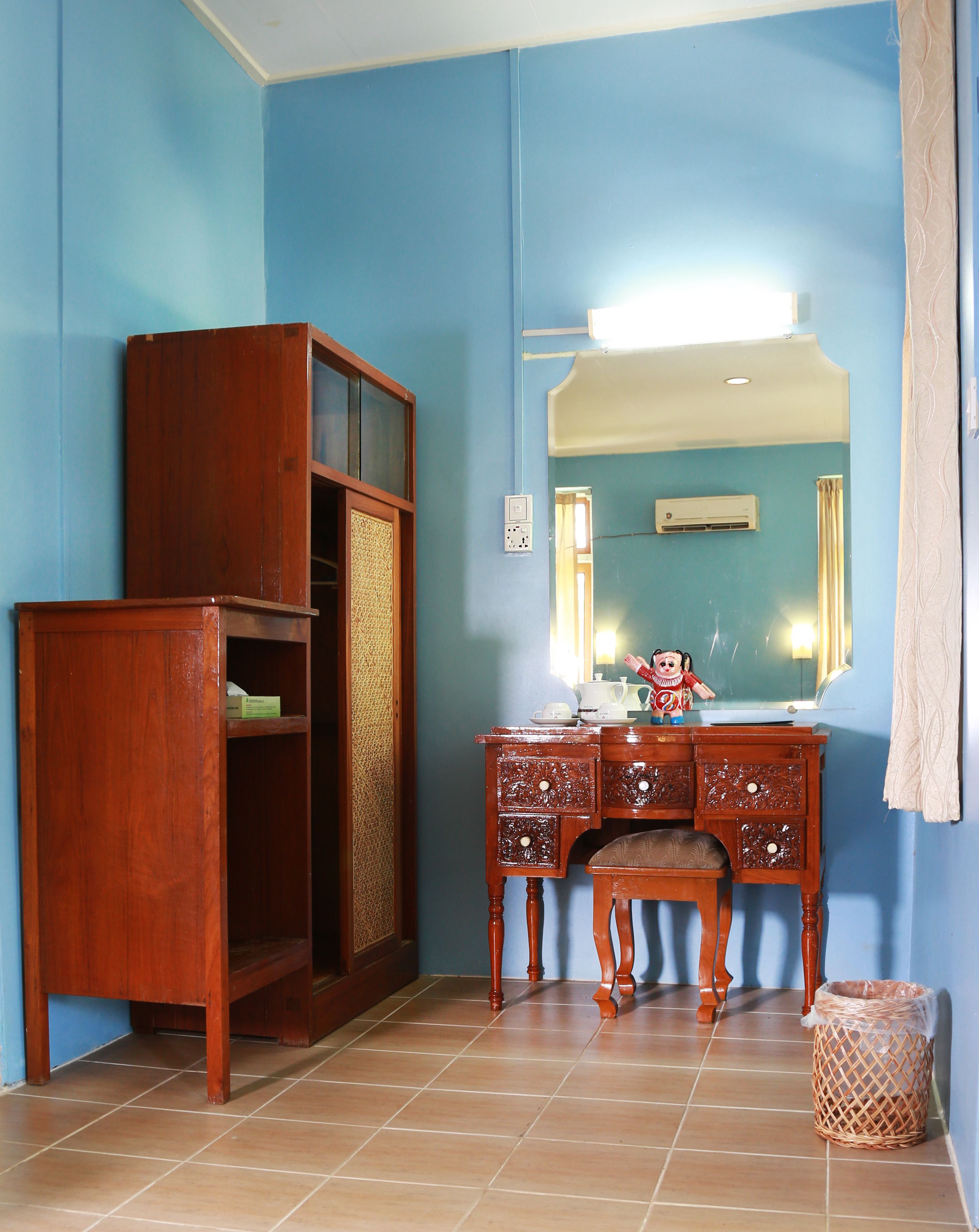 Una habitación con un armario de madera, un aparador con cajones, un espejo y suelo de baldosas.