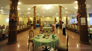 A spacious dining hall with multiple tables and chairs, large wooden pillars, and a ceiling with recessed lighting.