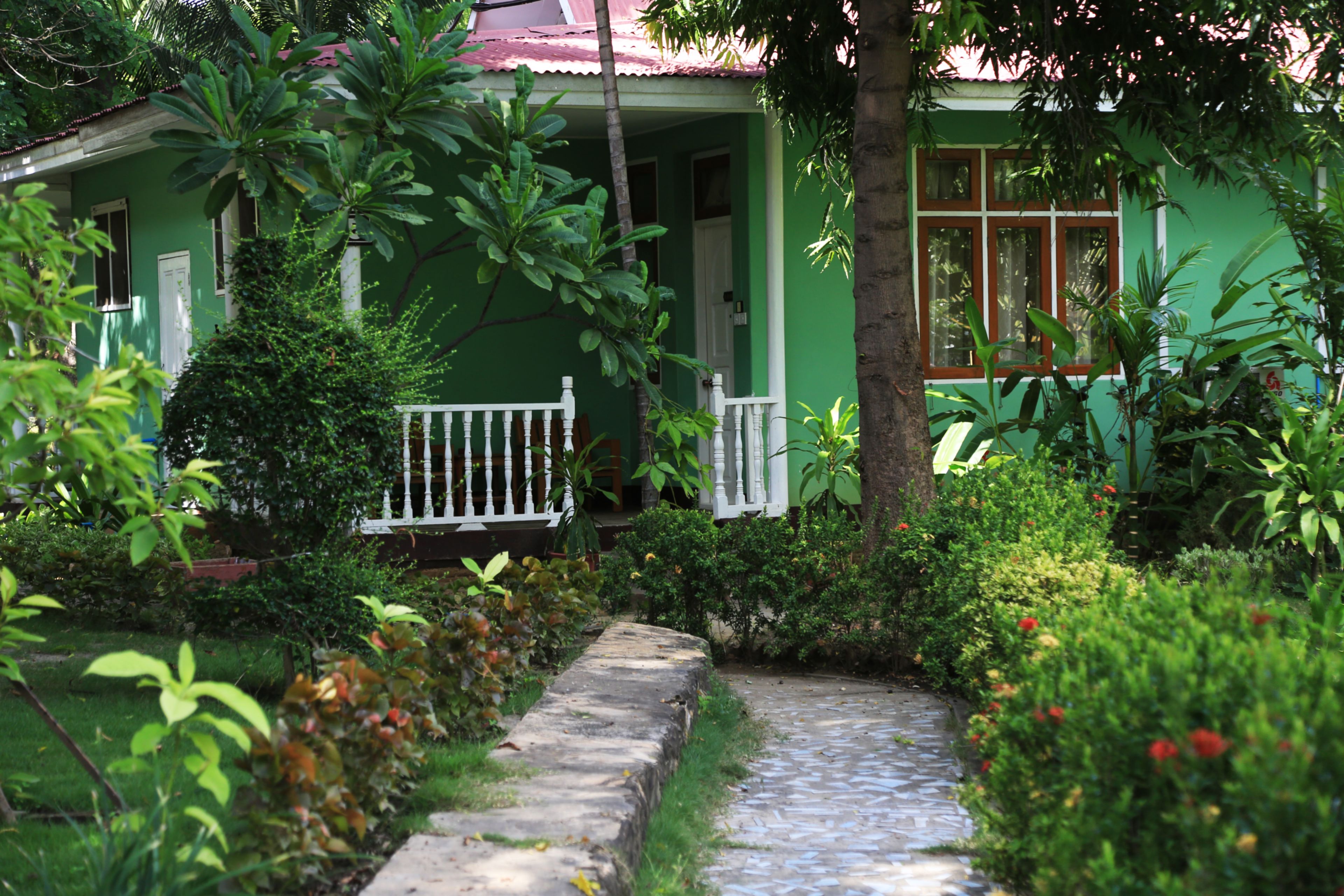 Una casa verde con un portico bianco e un vialetto in pietra che conduce all'ingresso.