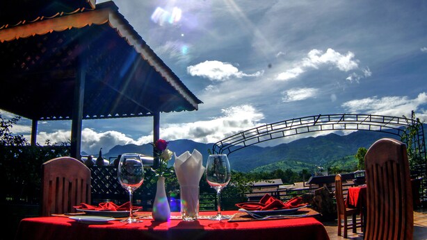 A table set for two with a red tablecloth, two wine glasses, a vase with flowers, and a red napkin.
